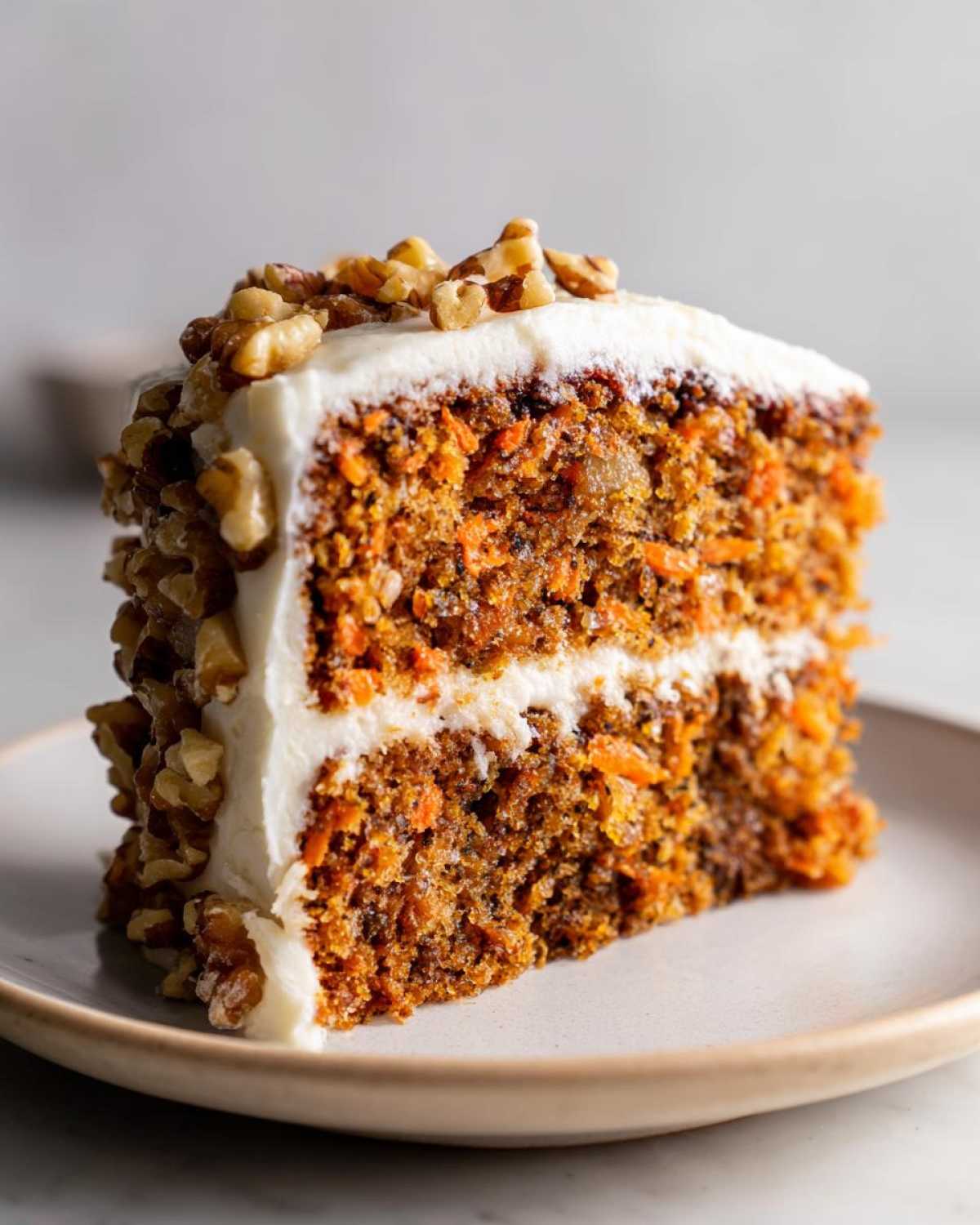 Zbliżenie na kawałek wilgotnego ciasto marchewkowe z orzechami i grubą warstwą białego kremu.