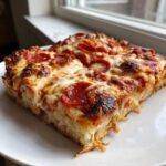 Zbliżenie na gruby kawałek Imprezowej pizzy z dużą ilością ciągnącego się sera i pepperoni.