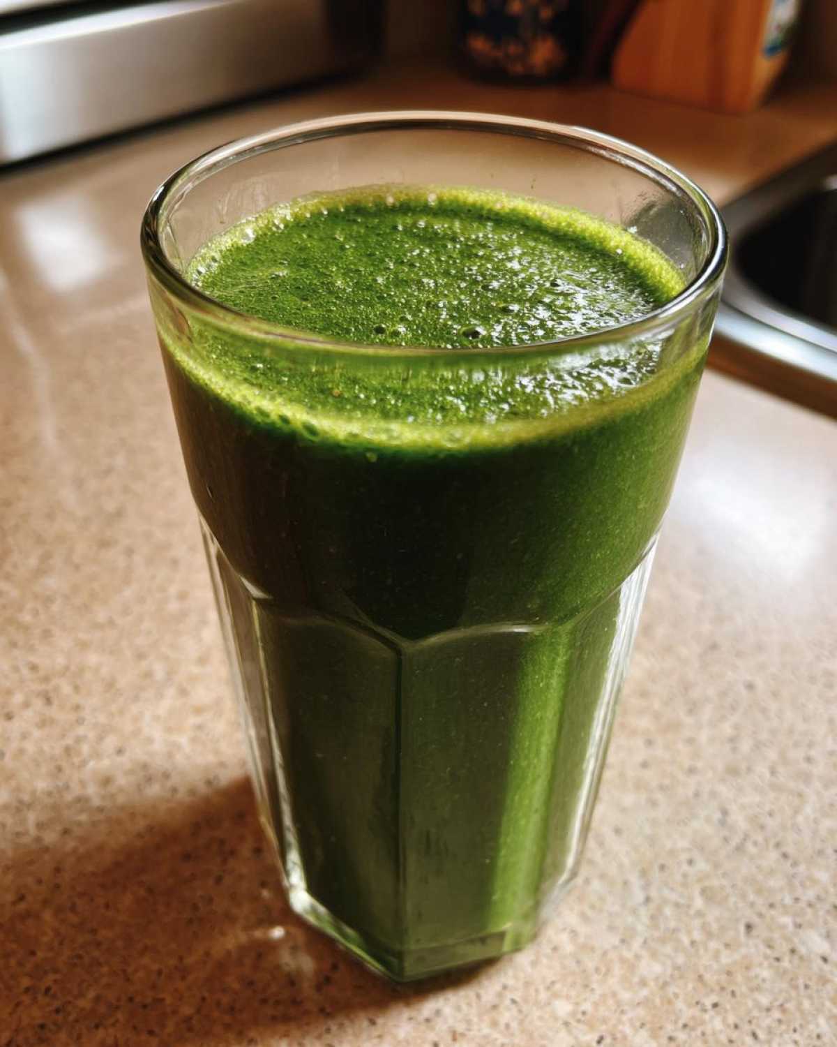 Zbliżenie na szklankę wypełnioną intensywnie zielonym Koktajl z jarmużu i jabłka z pianką na wierzchu.