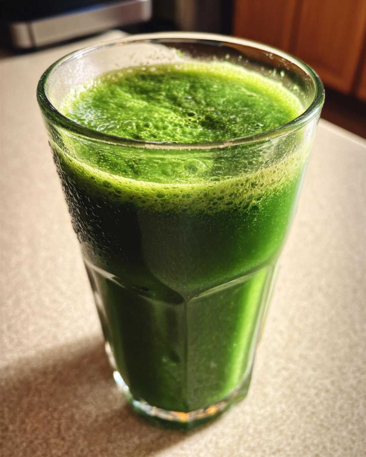 Zbliżenie na szklankę z intensywnie zielonym, spienionym Koktajl z jarmużu i jabłka.