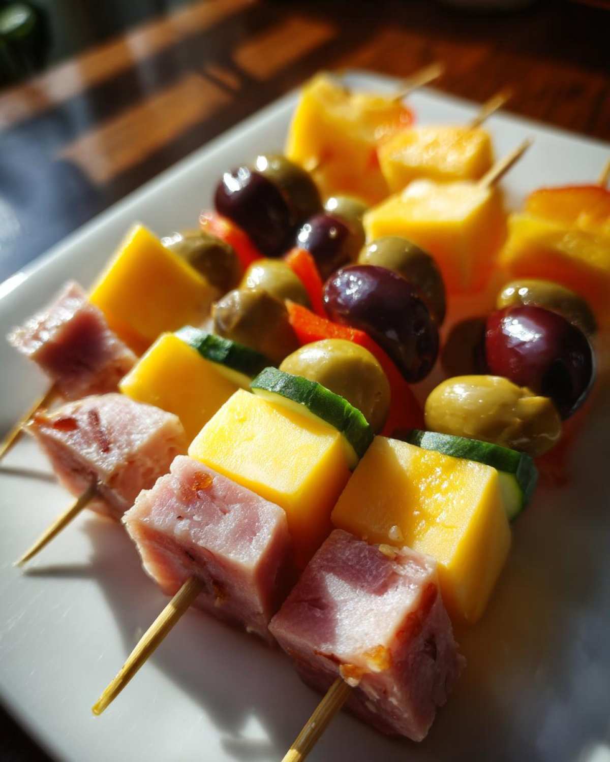 Zbliżenie na koreczki imprezowe nabite na patyczki: kawałki szynki, żółtego sera, ogórka i oliwek.