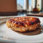 Zbliżenie na złocisty, usmażony kotlet mielony z pieczarkami, leżący na białym talerzu.