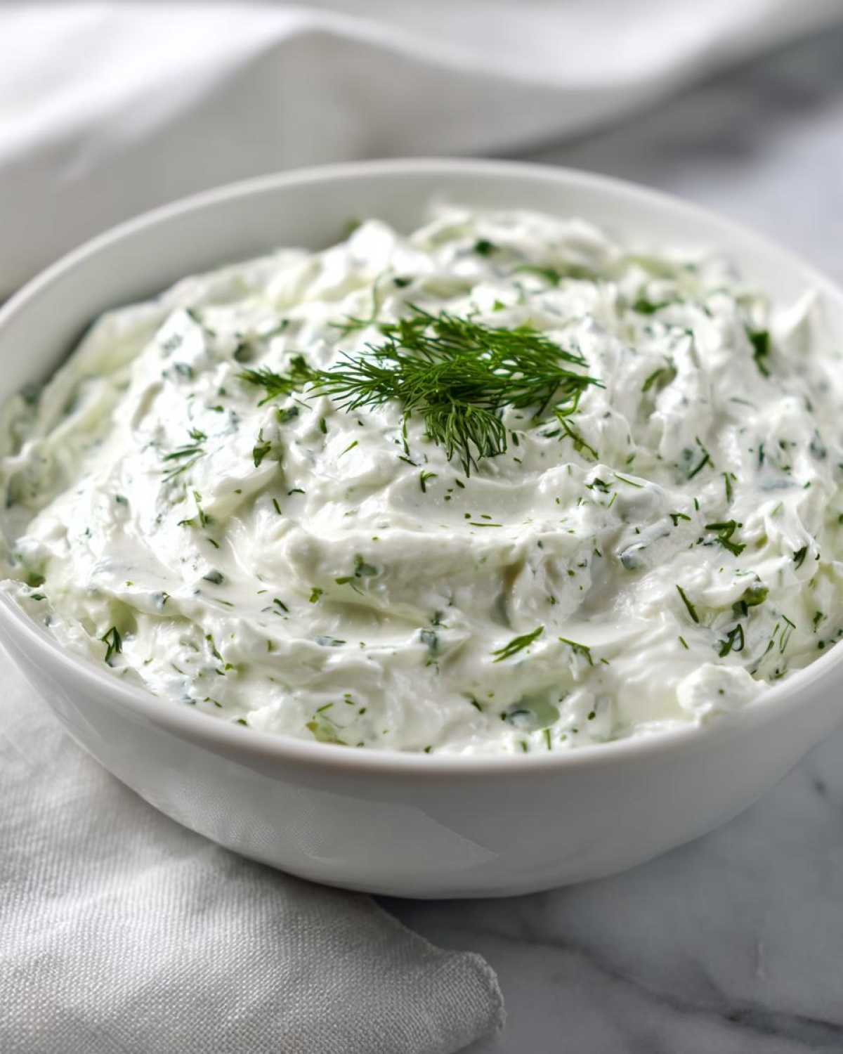 Zbliżenie na białą miskę wypełnioną kremowym, zielonym Dipem czosnkowym, udekorowanym świeżym koprem.