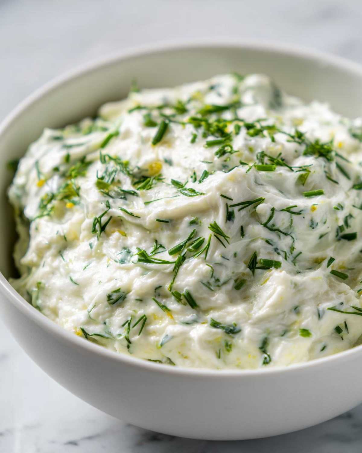 Zbliżenie na gęsty, biały dip czosnkowy udekorowany posiekanym szczypiorkiem i koperkiem.