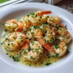 Zbliżenie na krewetki w sosie czosnkowym, obficie posypane świeżą pietruszką, podane w białym talerzu.