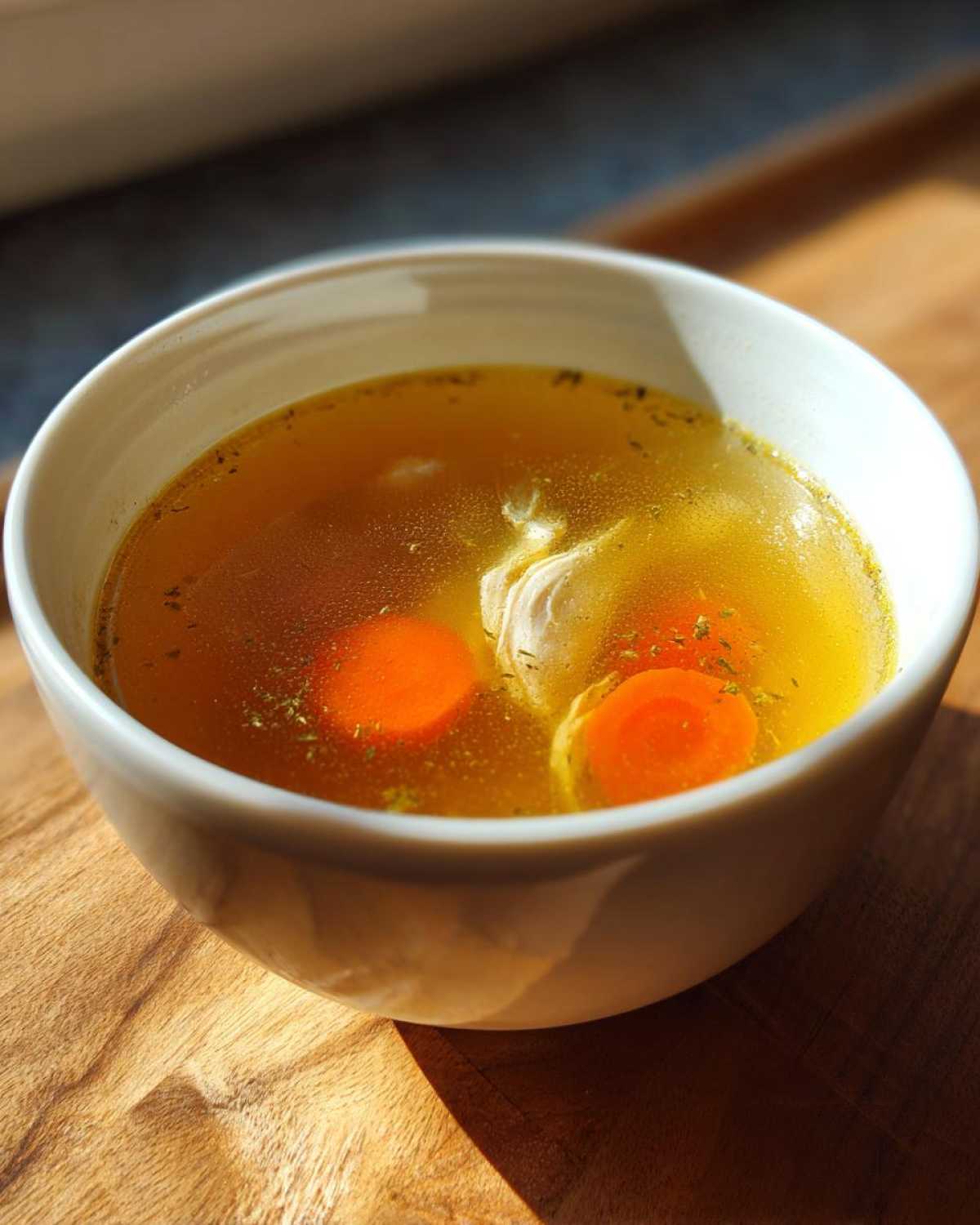 Zbliżenie na miseczkę Tradycyjny rosół z kury, z widocznymi plastrami marchewki i kawałkiem kurczaka.