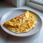 Złocisty omlet z kaszą jaglaną i kukurydzą na jasnym talerzu.