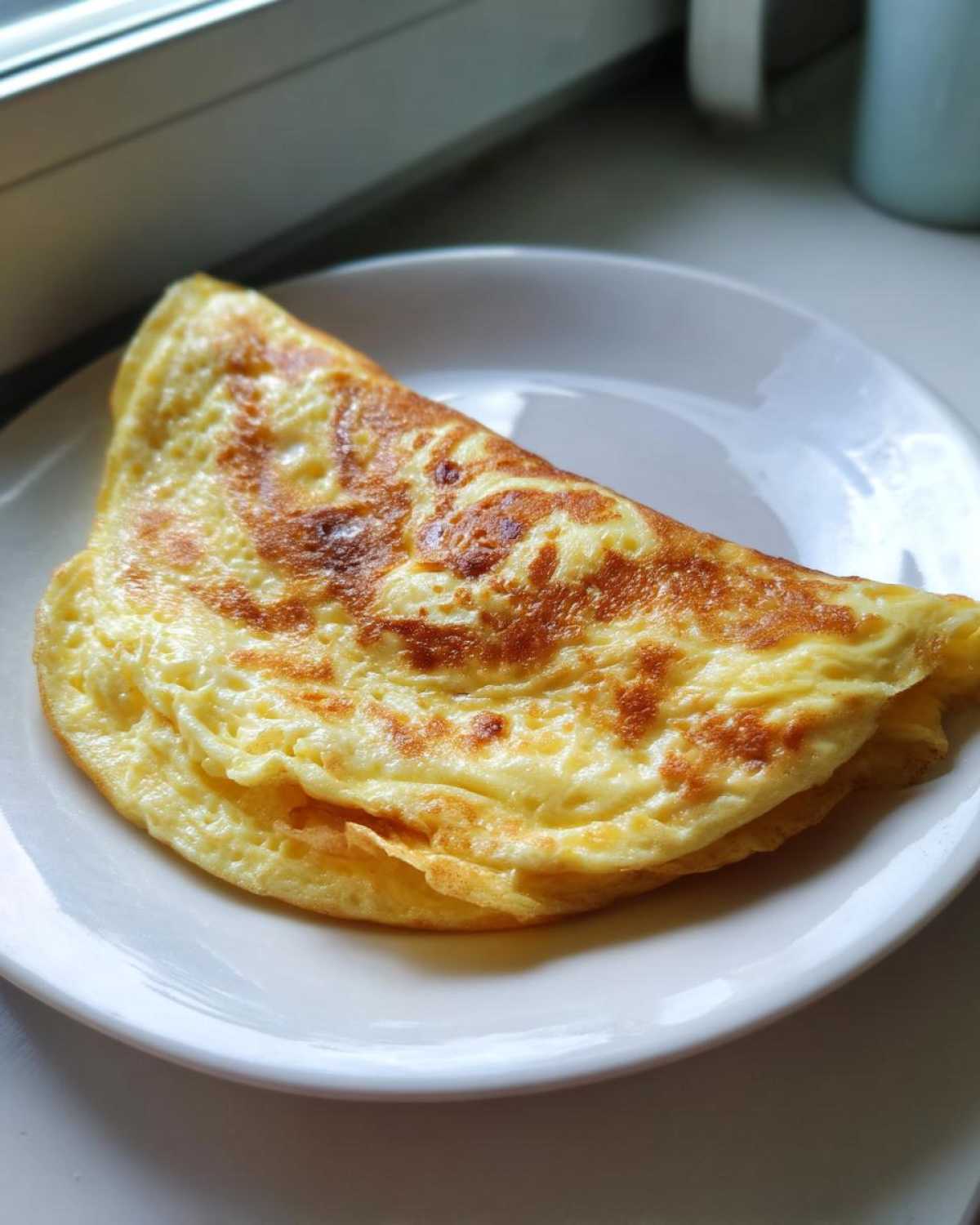 Złożony, puszysty omlet z kaszą jaglaną, lekko zrumieniony, podany na białym talerzu.