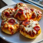 Zbliżenie na pięć małych, okrągłych pizzerinki z roztopionym serem i pepperoni, ułożone na białym talerzu.