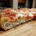 Zbliżenie na przekrój domowa pizza na grubym cieście, pokazujące puszysty środek i ciągnący się ser.