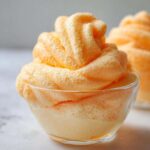 Zbliżenie na puszysty, pomarańczowy mus pomarańczowy nałożony na spód deseru w małej szklanej miseczce.