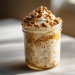 Słoik pełen kremowej owsianki nocnej z nasionami chia, zwieńczony jogurtem i chrupiącą granolą.