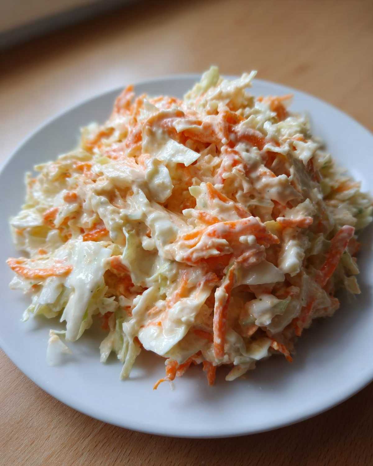 Zbliżenie na porcję kremowej sałatki coleslaw z tartą marchewką i kapustą na białym talerzu.