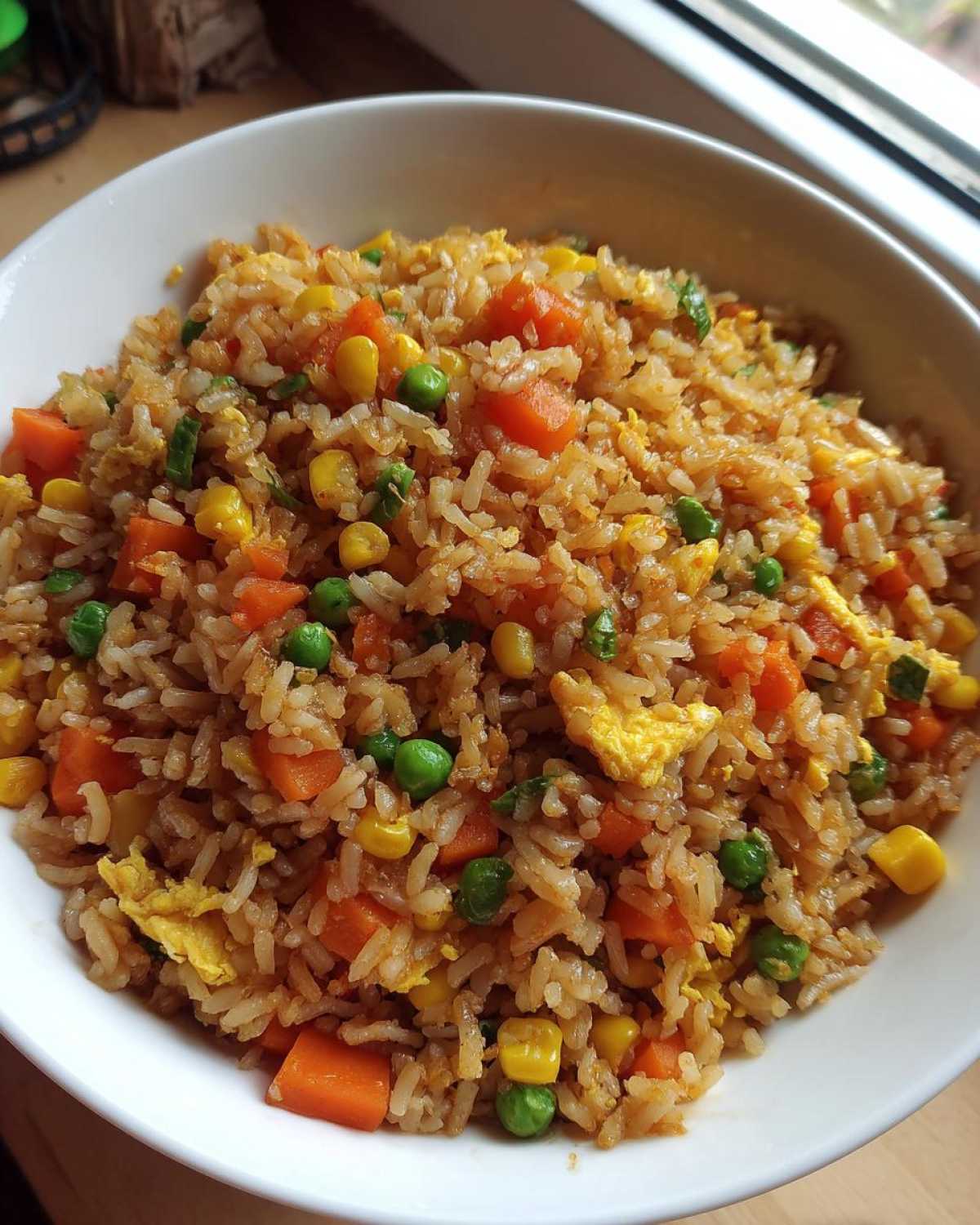 Zbliżenie na miskę pełną aromatycznego Ryż smażony z warzywami, z widoczną marchewką, groszkiem i jajkiem.