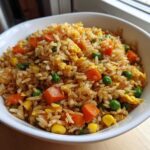 Zbliżenie na miskę pełną puszystego ryżu smażonego z warzywami, jajkiem, marchewką i groszkiem.