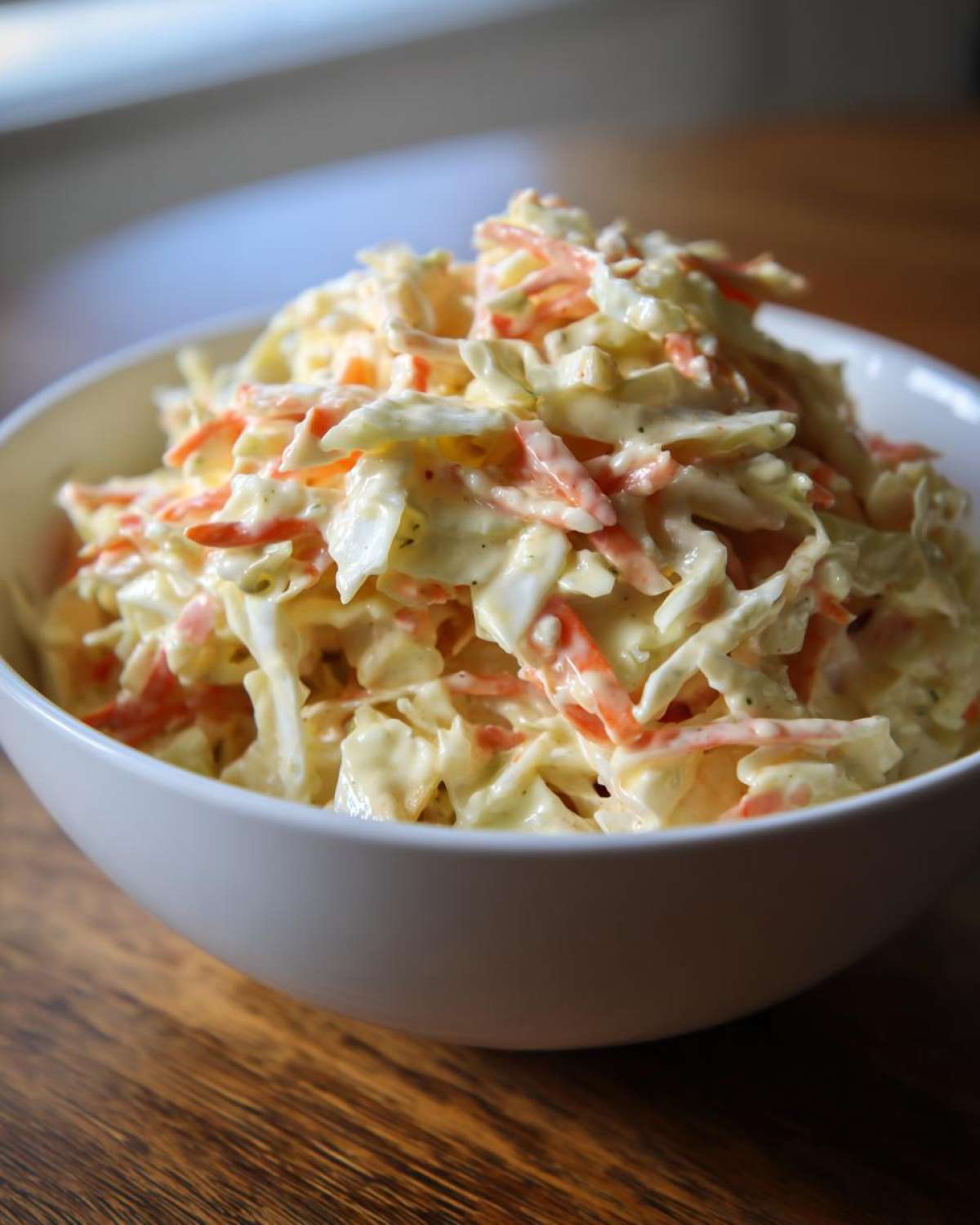 Zbliżenie na miskę pełną kremowej Sałatka Coleslaw domowa z tartą marchewką i kapustą.