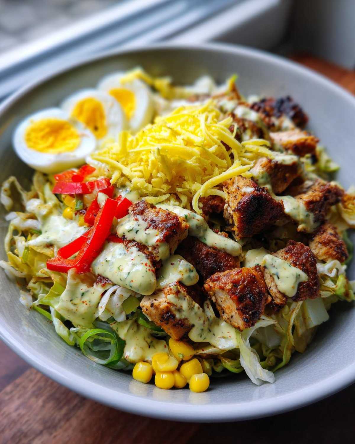 Zbliżenie na miskę pełną warstwowej Sałatki kebabowej z kawałkami grillowanego kurczaka, startym serem i jajkiem na twardo.