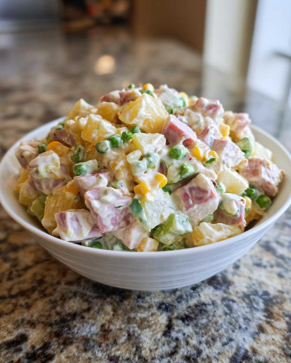 Zbliżenie na białą miskę pełną kremowej sałatki z selerem konserwowym, szynką, groszkiem i kukurydzą.