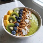 Zielony Smoothie bowl z owocami: kiwi, borówkami, mango, granolą i wiórkami kokosowymi.