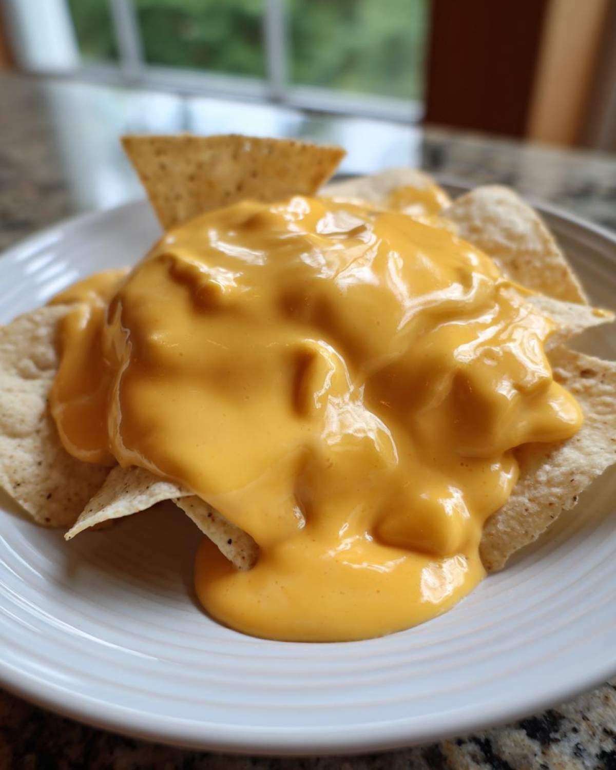 Zbliżenie na nachos polane obficie gęstym, kremowym sosem serowym do nachos na białym talerzu.