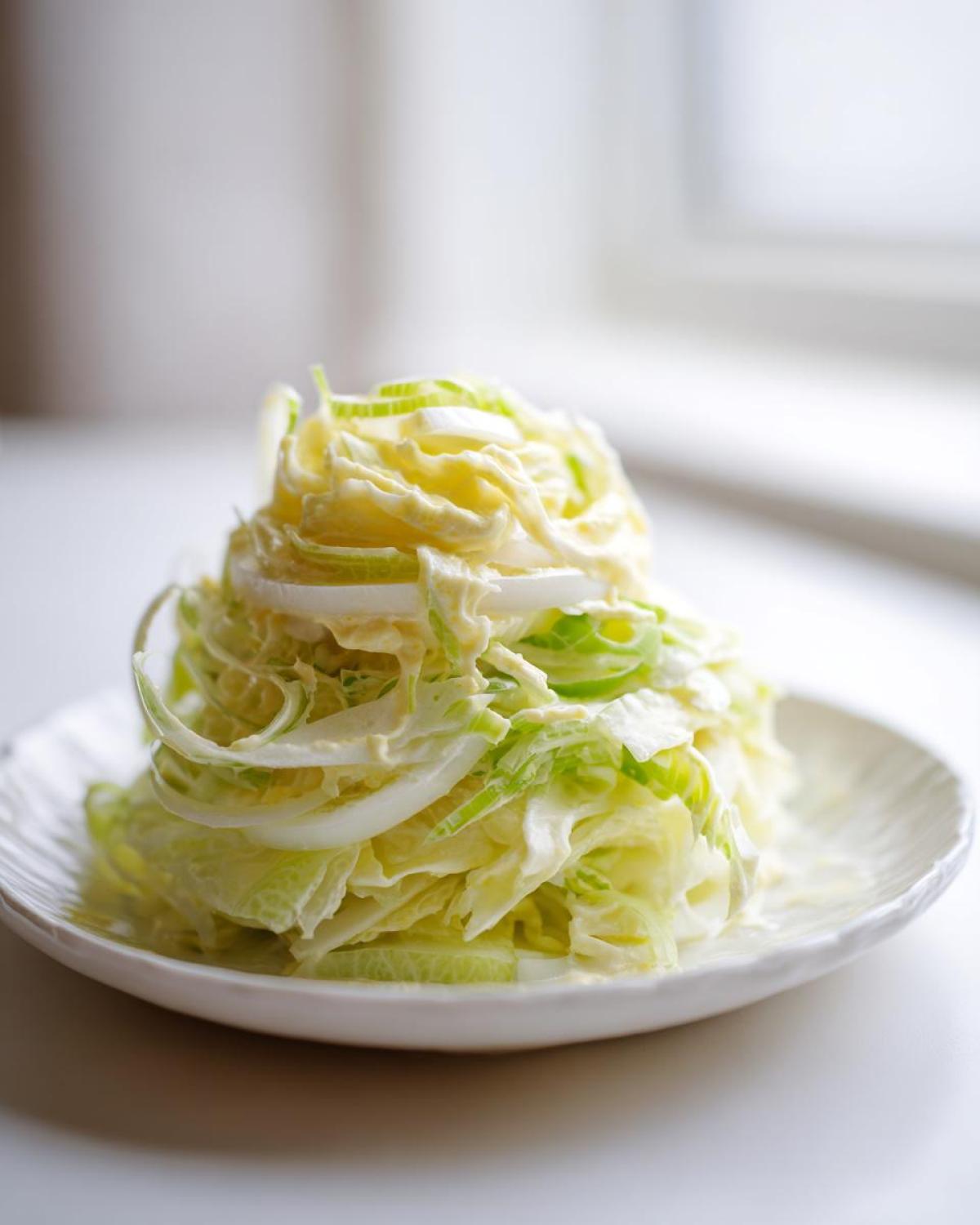 Wykwintna Surówka z pora z sosem majonezowym, ułożona na białym, ozdobnym talerzyku.