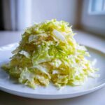 Kopiec chrupiącej surówki z pora w jasnym sosie majonezowym na białym talerzu.