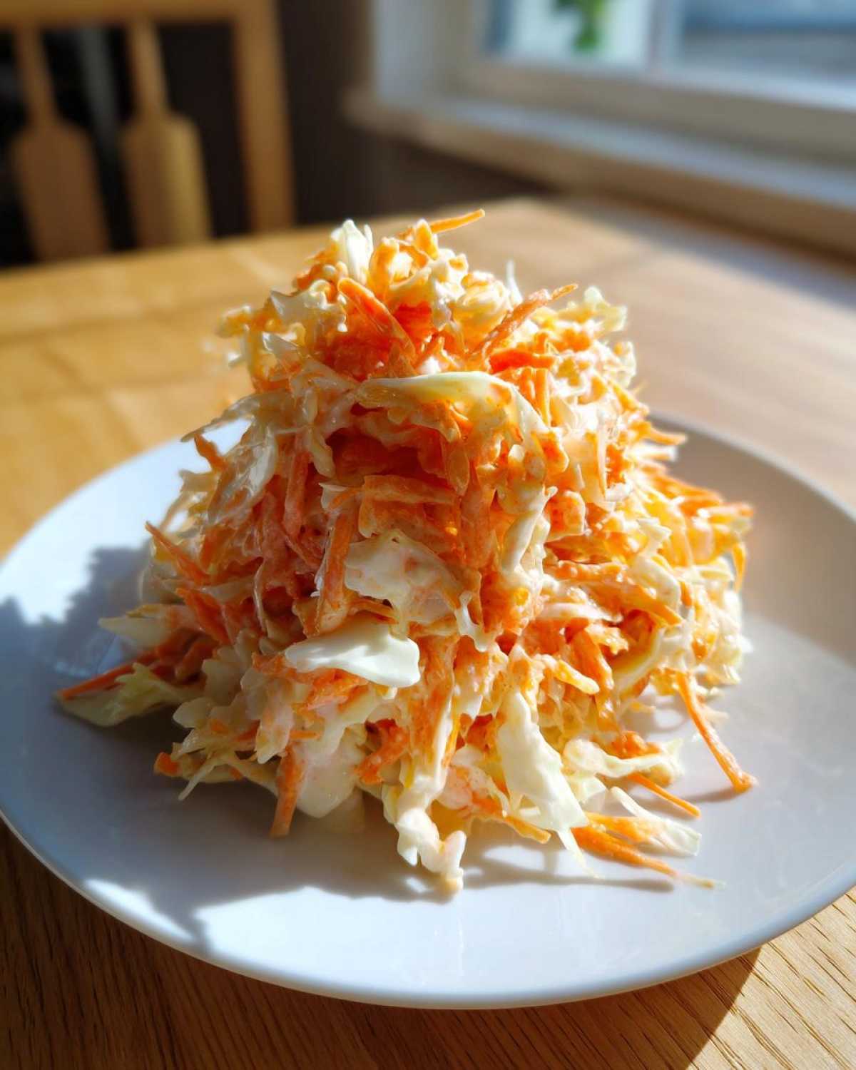 Porcja świeżej Sałatka coleslaw z tartą marchewką i kapustą w kremowym sosie na białym talerzu.