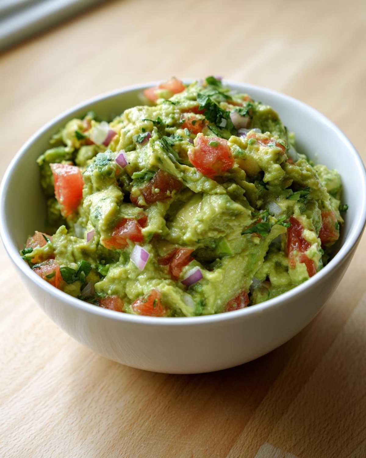 Zbliżenie na miskę z idealnym Guacamole klasyczne, widoczne kawałki awokado, pomidora i czerwonej cebuli.