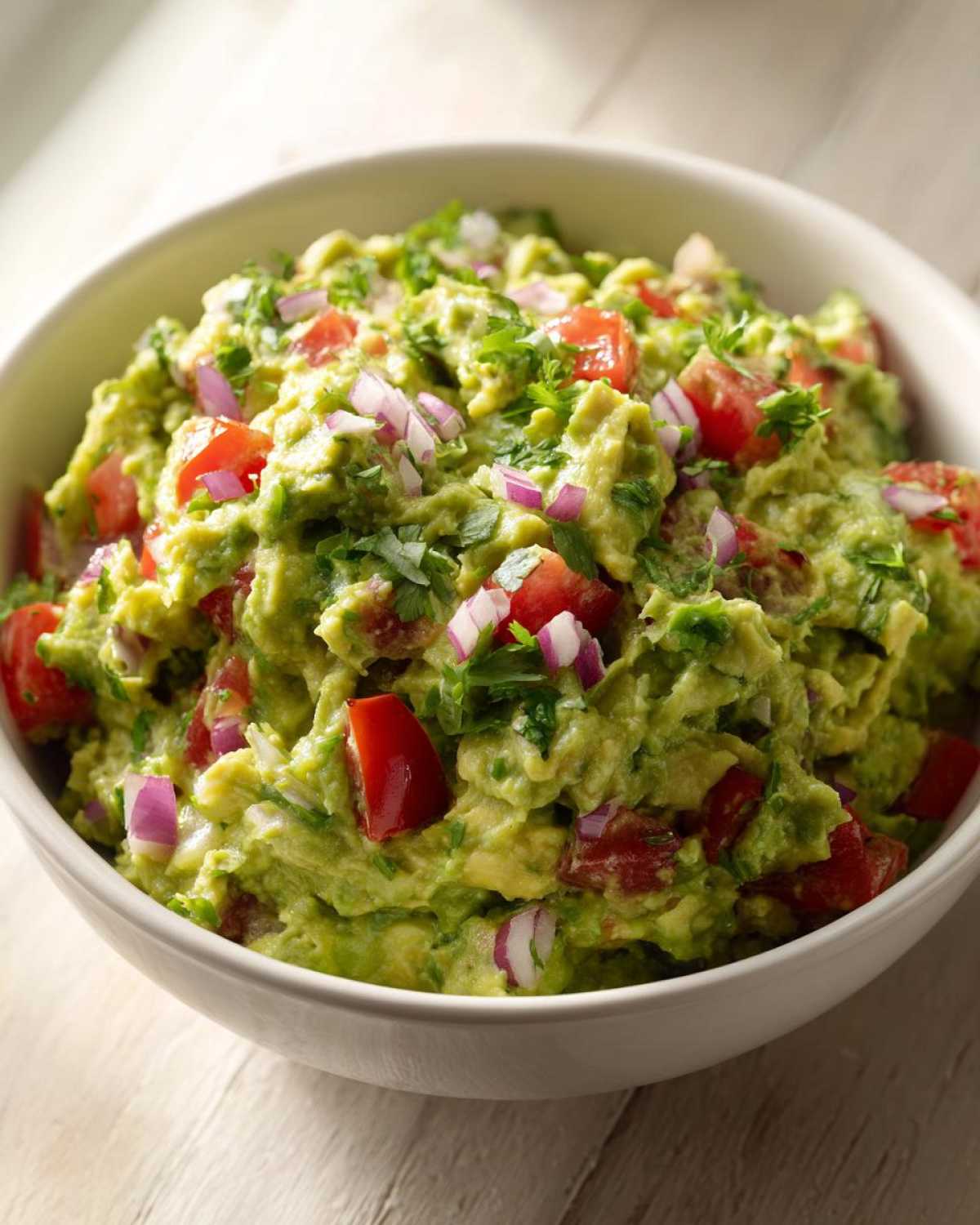 Zbliżenie na miskę pełną świeżego Guacamole klasyczne z kawałkami pomidora i czerwonej cebuli.
