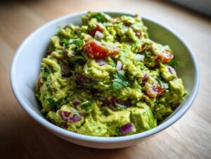 Zbliżenie na miseczkę pełną świeżego, grudkowatego Guacamole klasyczne z kawałkami pomidora i czerwonej cebuli.