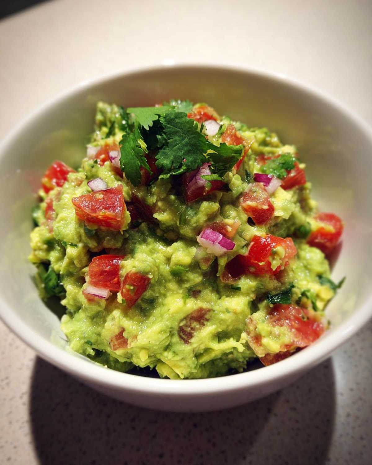 Zbliżenie na miseczkę świeżego, zielonego Guacamole z kawałkami pomidorów i cebuli.