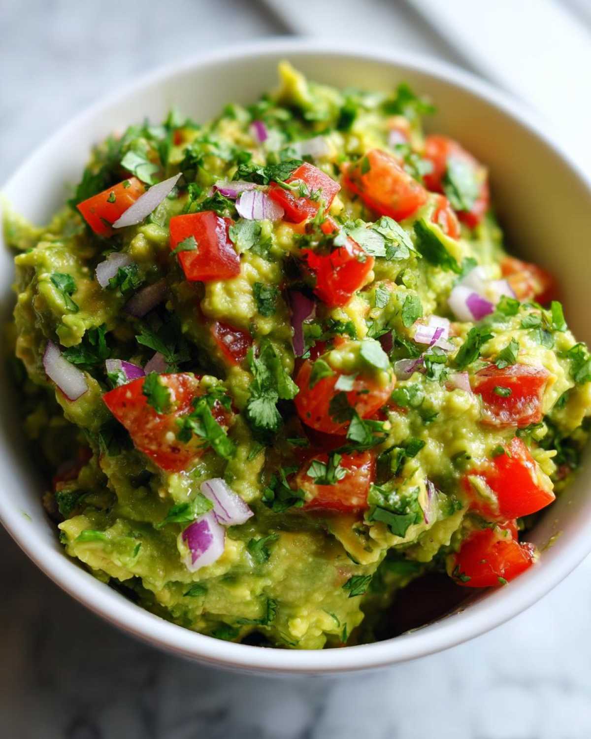 Zbliżenie na miseczkę świeżego Guacamole, posypanego kawałkami pomidora, czerwonej cebuli i kolendry.