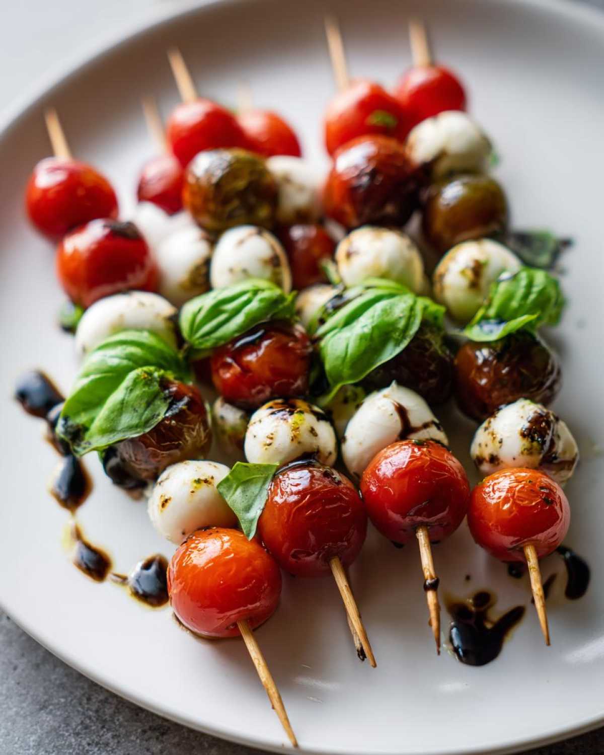 Zbliżenie na grillowane szaszłyki caprese z pomidorkami koktajlowymi, kulkami mozzarelli i liśćmi bazylii polane sosem balsamicznym.