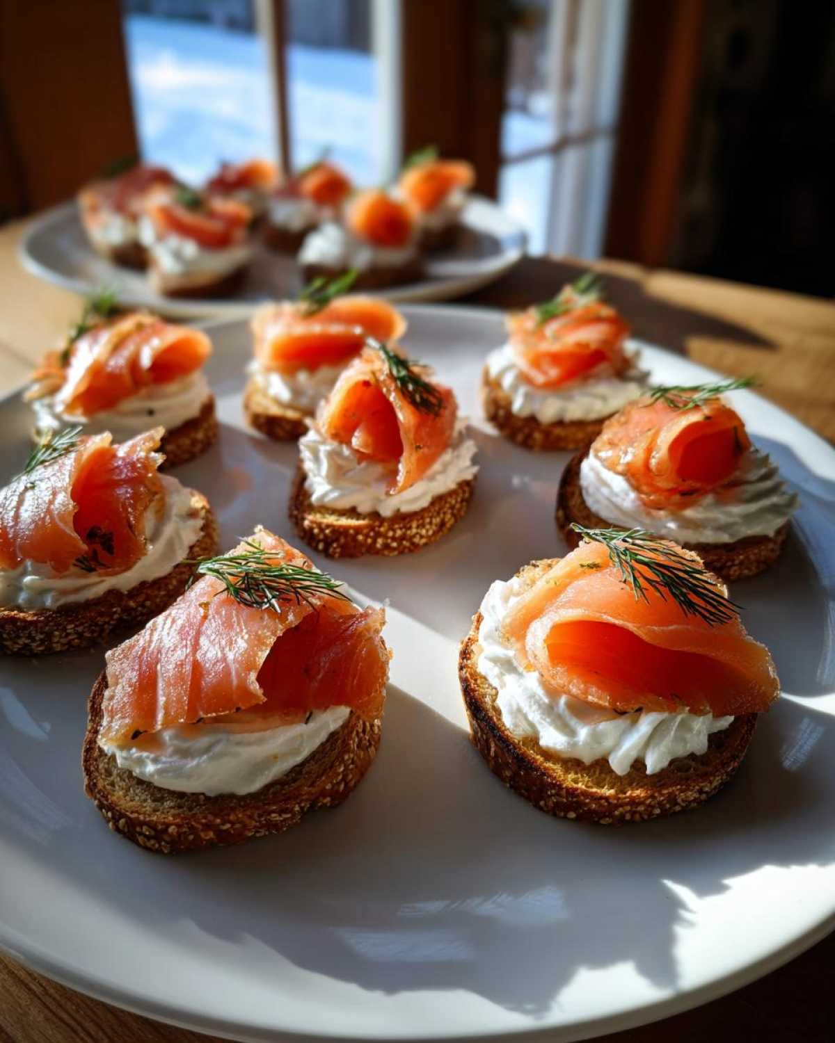 Kilka eleganckich tartinek z łososiem, serkiem i koperkiem na białym talerzu. Idealne tartinki z łososiem.