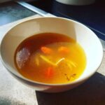 Zbliżenie na miskę Tradycyjny rosół z kury z kawałkami marchewki i makaronem, o intensywnym złotym kolorze.