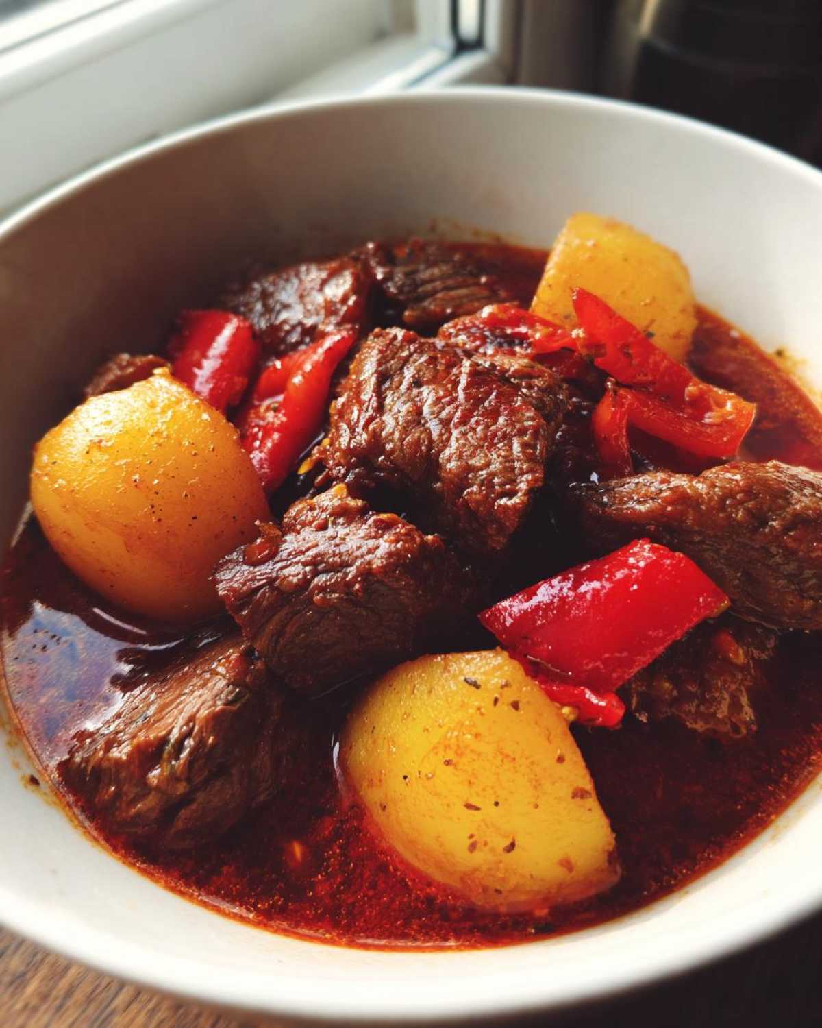 Zbliżenie na miskę aromatycznej Zupa gulaszowa węgierska z dużymi kawałkami wołowiny, żółtymi ziemniakami i czerwonymi paprykami.