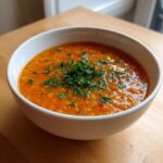 Zbliżenie na miskę pełną gęstej, pomarańczowej zupy pomidorowej z soczewicą, posypanej świeżą natką pietruszki.