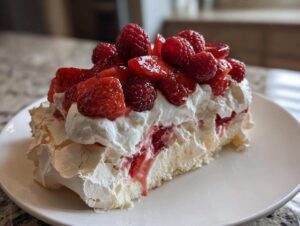 Kawałek Beza Pavlova z owocami, bitą śmietaną i świeżymi truskawkami oraz malinami na białym talerzu.