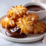 Chrupiące churros z sosem czekoladowym, jedno z nich jest zanurzone w gęstej czekoladzie.