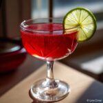 Zbliżenie na kieliszek z intensywnie czerwonym, musującym drinkiem walentynkowym, udekorowanym plasterkiem limonki.