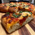Zbliżenie na kawałek puszystej pizzy domowej margarita z ciągnącym się serem i bazylią na desce.