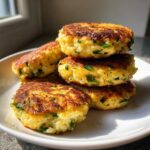 Stos usmażonych kotletów jajecznych ze szczypiorkiem, złocistych i puszystych, na białym talerzu.
