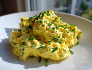Kremowa, żółta pasta jajeczna na kanapki obficie posypana posiekanym zielonym szczypiorkiem, podana na białym talerzu.