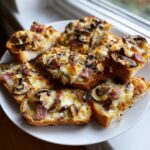 Talerz pełen chrupiących Mini zapiekanki z bagietki z roztopionym serem, pieczarkami i szynką.