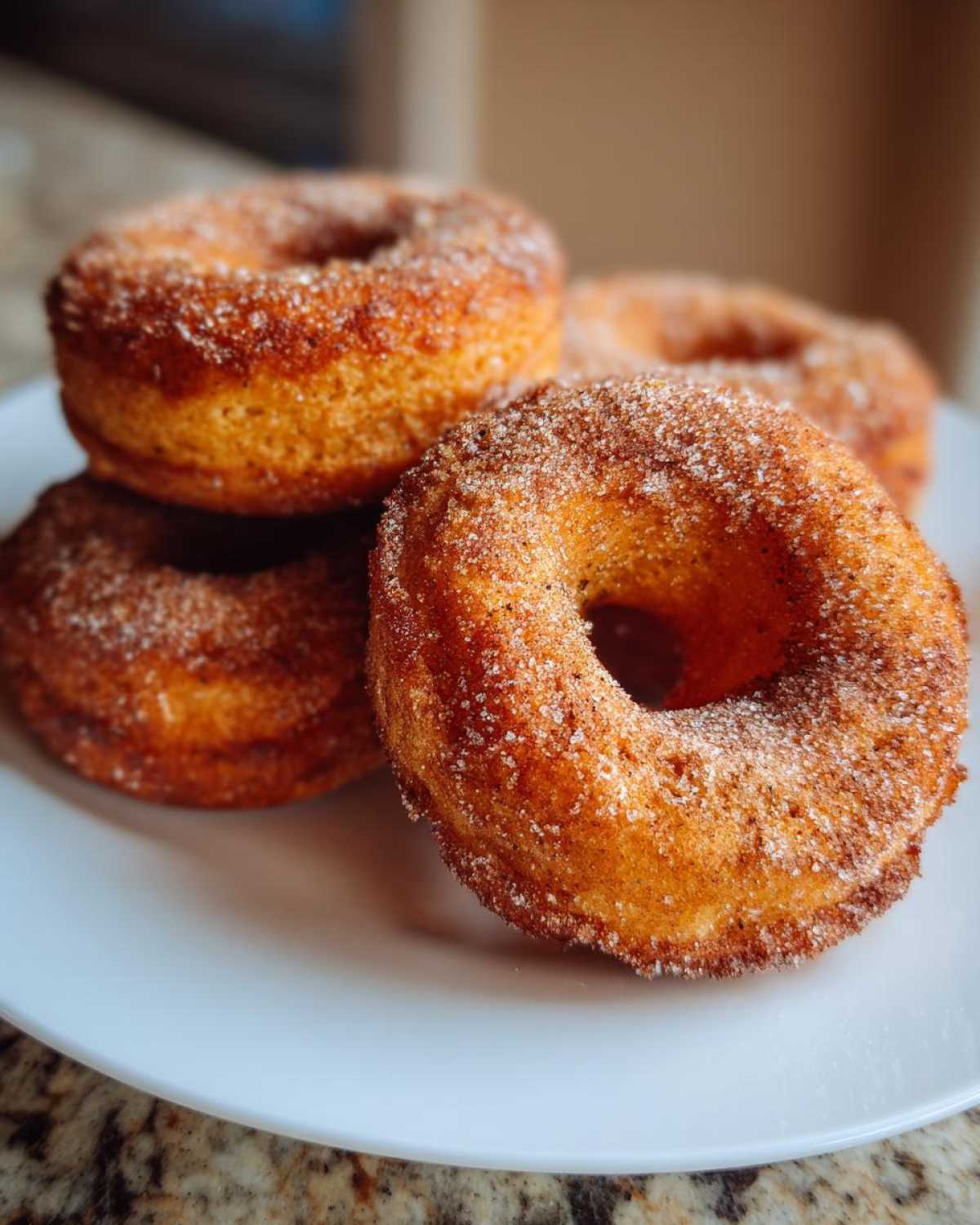 Zbliżenie na stos pączków keto z mąki kokosowej, obficie posypanych cukrem cynamonowym na białym talerzu.