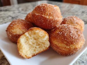 Keto pączki z mąki kokosowej, złociste i obtoczone w cukrze, z jednym przekrojonym na pół.