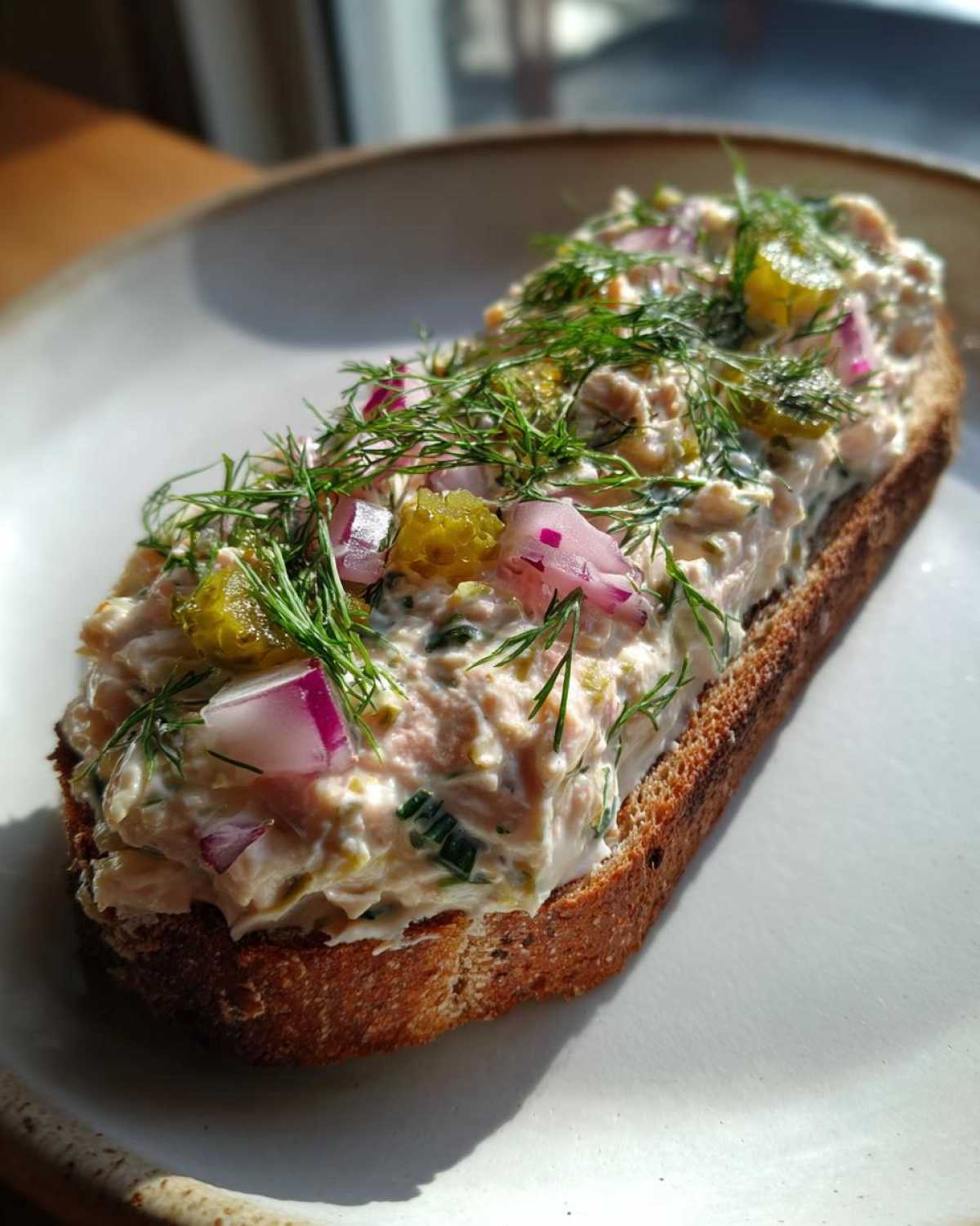 Kanapka z grubą warstwą pasty z makreli wędzonej, udekorowana koperkiem, czerwoną cebulą i ogórkiem kiszonym.
