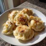 Talerz pełen ugotowanych i podsmażonych Pierogi ruskie domowe, polane złocistą cebulką.