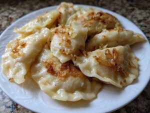 Zbliżenie na talerz pełen domowych Pierogi ruskie domowe polane skarmelizowaną cebulką.