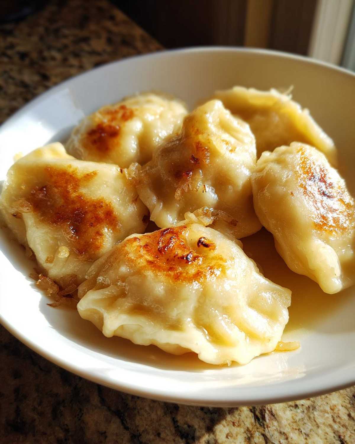 Zbliżenie na talerz pełen podsmażanych pierogi ruskie domowe polane tłuszczem i cebulką.